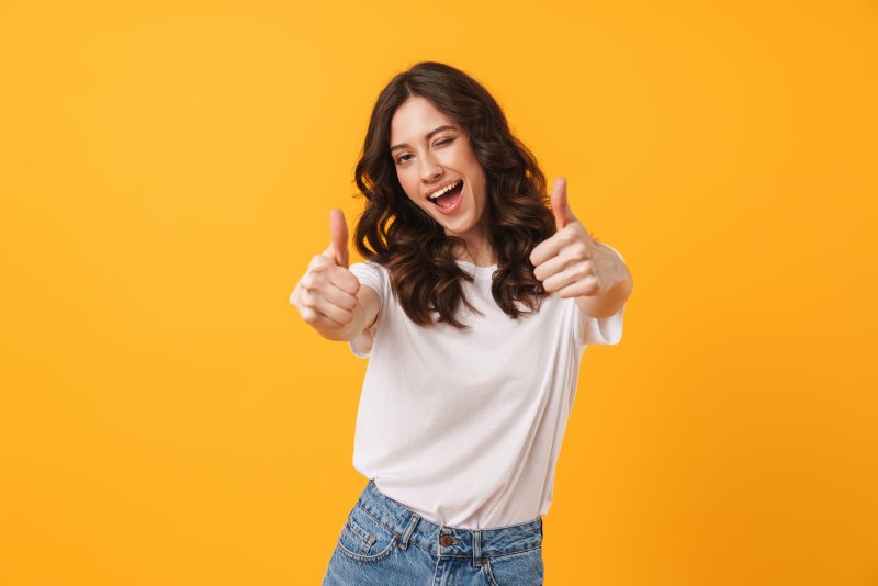 woman smiling and giving a thumbs up in front of a yellow background